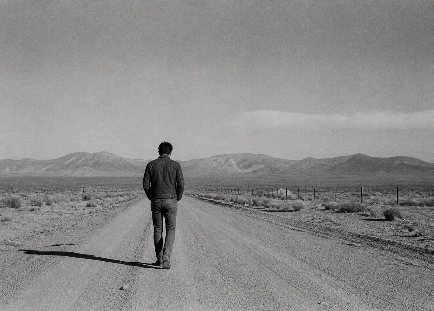 A lone figure in denim walking a dusty desert road, 1960s film photograph